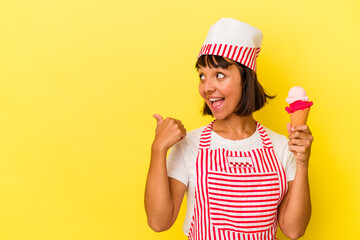 Young mixed race ice cream maker woman holding an ice cream isolated on yellow background points with thumb finger away, laughing and carefree.