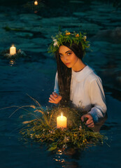 Pagan goddess. water lake, ritual flower wreaths float, candles burning. girl swims in riwer. white...