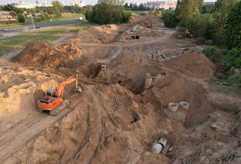 Laying of underground storm sewer pipes and sewerage well. Excavator at construction of water main, sanitary sewer, storm drain systems. Aerial view of the concrete pipe and concrete wells
