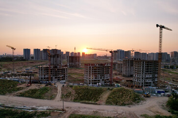 Obraz premium Tower cranes in action at construction site on sunset background. Arial view of the crane the conctruct the high-rise building. New residential skyscraper. Tall house renovation project