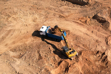 Excavator load the sand into dump truck. Aerial view of an backhoe on earthworks. Open pit development and sand mining. Loader digging ground for foundation pit. Earthmoving at construction site. © MaxSafaniuk