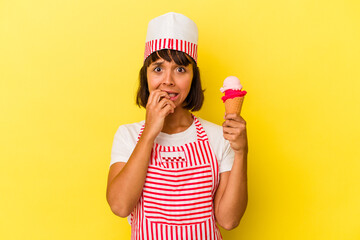 Young mixed race ice cream maker woman holding an ice cream isolated on yellow background biting fingernails, nervous and very anxious.