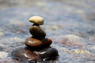 Fototapeta na wymiar Pyramid of wet pebbles in the sea waves. Summer vacation, beach stones, balance and relax concept