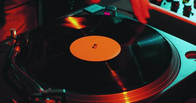 Deejay spinning vinyl musical record on turntable during dj rave, close-up. Nightlife and music