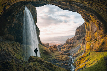 Adventurous young man standing behind waterfall in the highlands of Iceland. High quality panorama...
