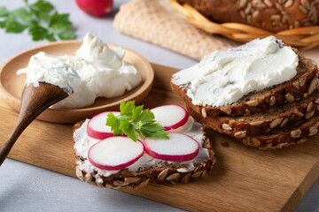 Home made rye bread on a wooden cutting board with curd cheese, radish and ricotta and herbs....