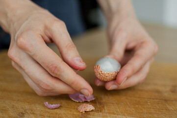 Female hands hold a litchi fruit, lychee on a wooden desk. Exotic fruits, healthy eating concept