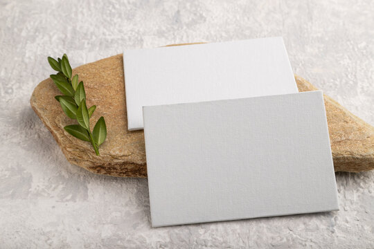 White paper business card, mockup with stone and boxwood branch on gray concrete background. side view, copy space.