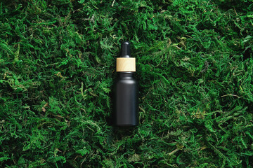 Black dropper serum bottle on moss background, top view. Natural organic cosmetics concept.