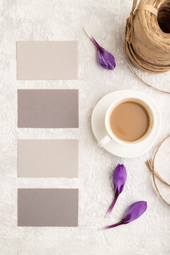 Gray paper business card mockup with spring snowdrop crocus flowers and cup of coffee on gray concrete background. top view, copy space.