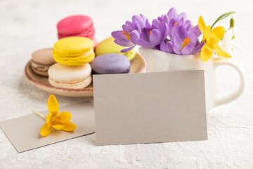 Gray paper business card mockup with spring snowdrop crocus flowers and multicolored macaroons on gray concrete background. side view, copy space.