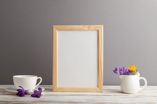 Beige wooden frame mockup with snowdrop crocus flowers and white coffee cup on gray paper background. still life, copy space.