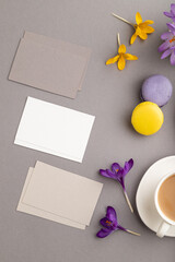 Gray and white business card mockup with spring snowdrop crocus flowers, cup of coffee, multicolored macaroons on gray pastel background. top view, copy space.