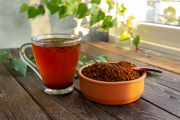 A cup of chaga tea on a dark table. Chaga slices and birch twig