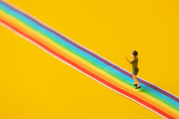 little boy figure stand on rainbow LGBT strip on yellow background - obrazy, fototapety, plakaty