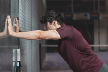 a young paddle tennis player stretched out his arms on the wall. ©  Yistocking