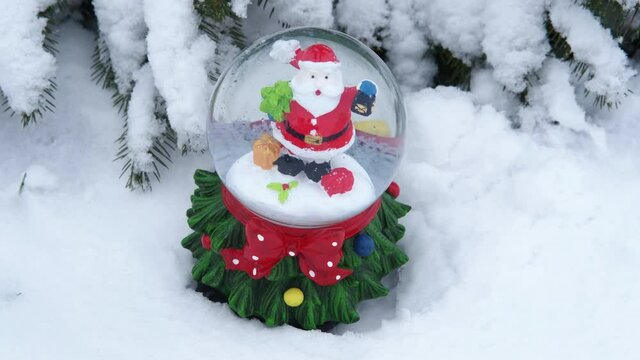 Mood with a Christmas globe. A view of a joyful Santa Claus in the Christmas globe in the forest with snow.