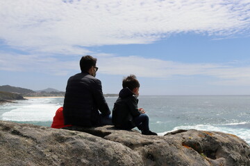 Fototapeta na wymiar Father and young son sitting on a rock looking out to sea.