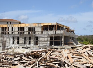 Messy construction site, with scrap wood in the foreground, half finished block building with scaffolding in the background