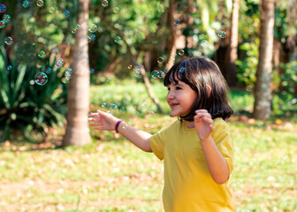 Beautiful brazilian child girl wearing yellow plays with soap bubbles outdoors with nature in the background