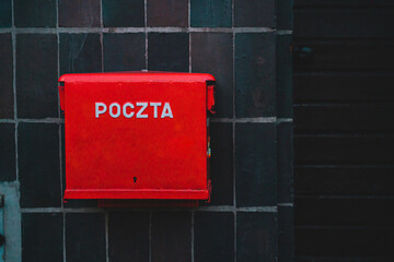 Red polish post office box installed on the facade of the black building. Poczta Polska. Mail. Outdoor. City. Street