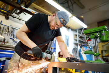 Metalwork craftsman cutting metal with grinder tools. Worker man in protection gloves and glasses working in the workshop. Small local business.