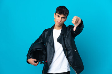 Naklejka premium Young man with a motorcycle helmet over isolated blue background showing thumb down with negative expression