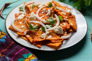 Mexican food. Red chilaquiles with cheese and sour cream on turquoise background