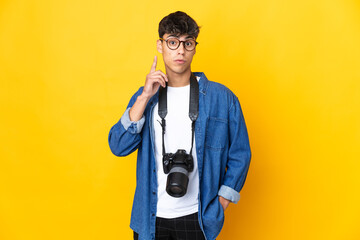 Young photographer man over isolated yellow background thinking an idea pointing the finger up