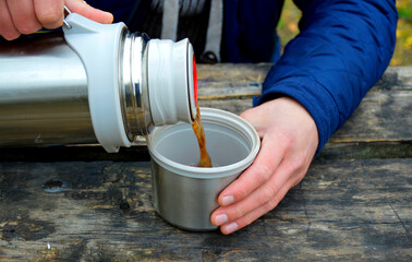 one man's hand holds a mug, the other pours a drink, tea from a thermos in nature