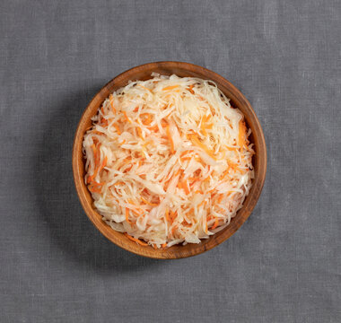 Sauerkraut in a wooden bowl on a gray background close up. Fermented food. Cabbage salad with carrots. Top view, flat lay.