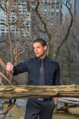 Fototapeta premium Dressing in a black shirt, tie, a young handsome guy is pondering at small woods in winter.