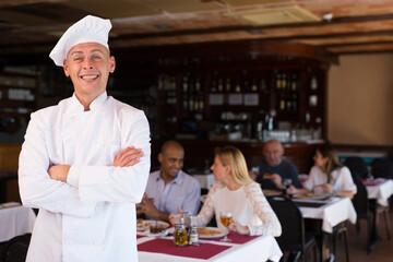 Portrait of happy chef with crossed arms in restaurant hall