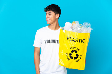 holding a bag full of plastic bottles to recycle over blue background looking side