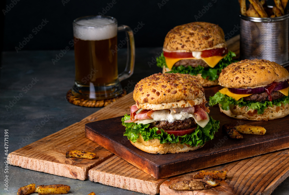 Wall mural Closeup of delicious beef burgers served on two wooden boards with beer and fries in the background