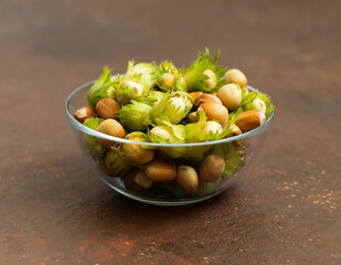 Hazelnuts in a bowl on a brown background. Nuts with green leaves. Filbert closeup.