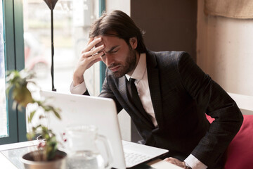 Young businessman sitting at a coffeehouse, having a headache