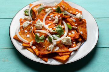 Mexican food. Red chilaquiles with cheese and sour cream on turquoise background