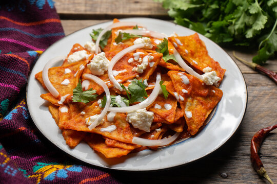 Mexican food. Red chilaquiles with cheese and sour cream on wooden background