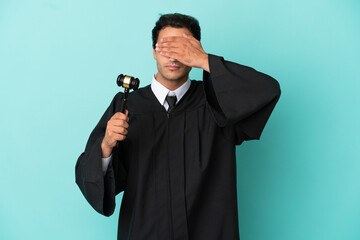 Judge over isolated blue background covering eyes by hands. Do not want to see something