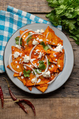 Mexican food. Red chilaquiles with cheese and sour cream on wooden background