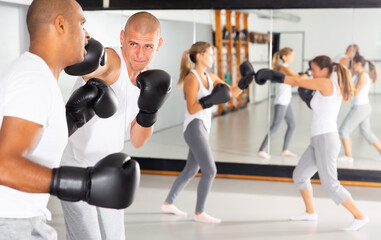 Active man wearing boxing gloves sparring during self-defense course at gym, practicing effective...