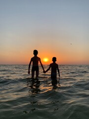 Children hold hands standing in the sea against the sunset. Children's rest on the beach at the sea. The boys are swimming in the sea.