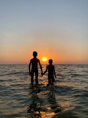Children hold hands standing in the sea against the sunset. Children's rest on the beach at the sea. The boys are swimming in the sea.