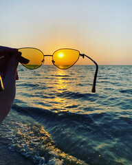 Sunglasses with yellow glasses on the background of the sunset over the sea.