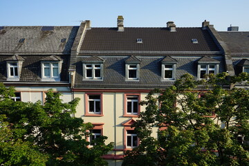 Fototapeta na wymiar Blick aus dem Dachfenster über grüne Alleebäume auf sanierte Dächer mit Dachwohnung, Gaube und Mansarde von Altbauten im Nordend von Frankfurt am Main in Hessen