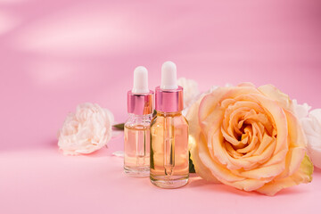 Obraz na płótnie Canvas Essential rose oil in cosmetic bottle near fresh rose flowers against pink background.