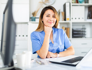 Woman doctor in uniform is working behind laptop in clinic