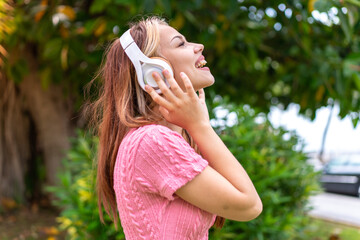 Young pretty woman at outdoors listening music and singing