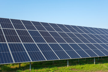 Row of solar panels on a solar farm under a blue sky.